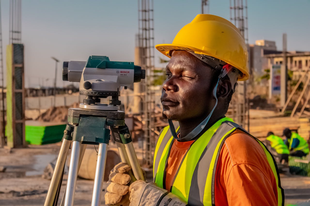 A construction worker using a theodolite for land surveying at a building site.