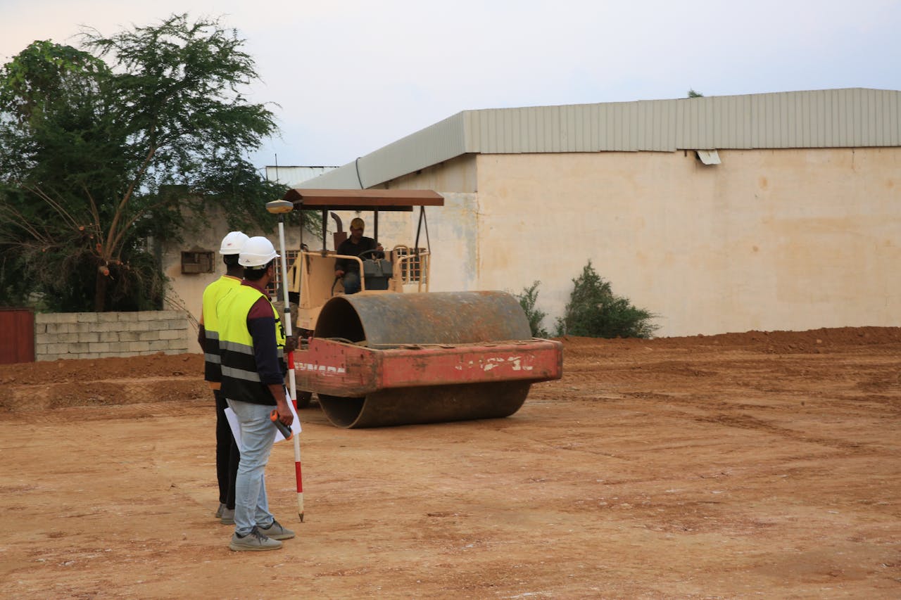 Engineers in high-visibility vests supervise road construction with a roller.