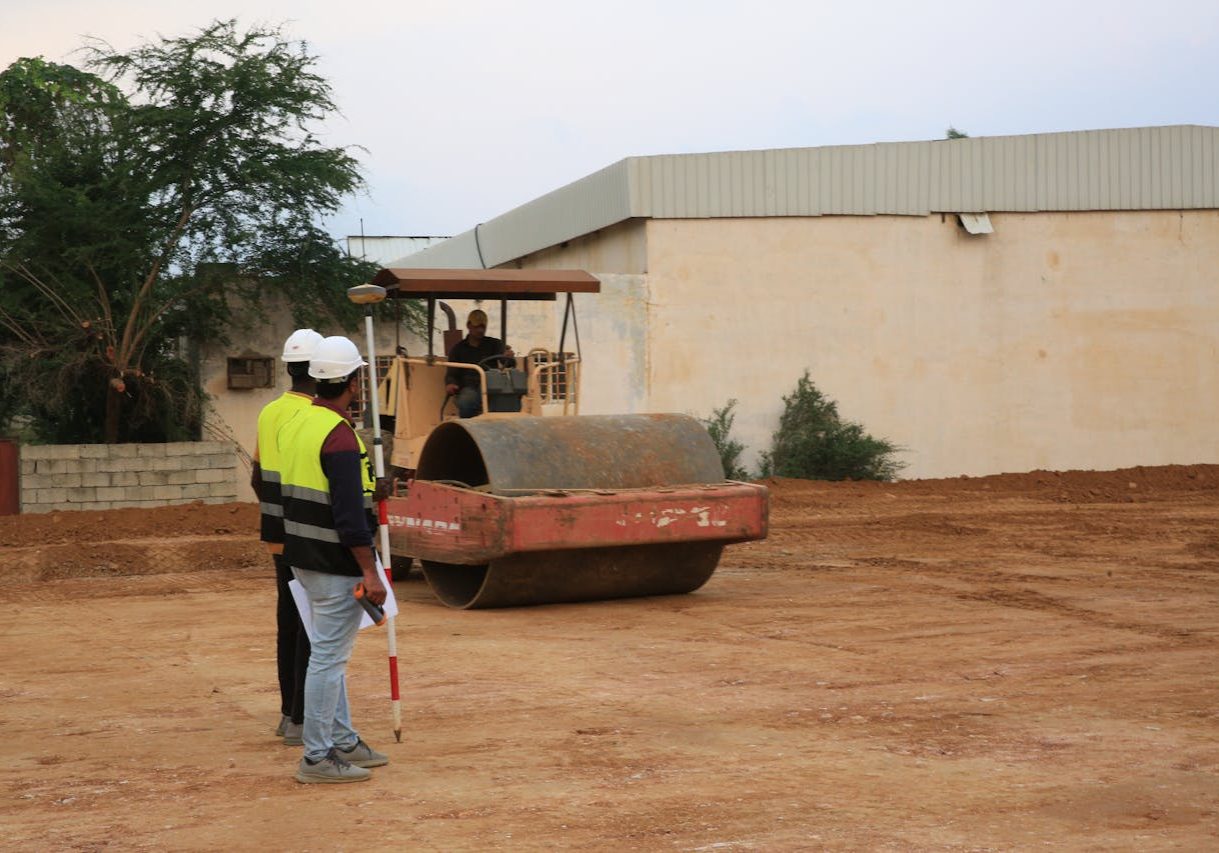 Engineers in high-visibility vests supervise road construction with a roller.